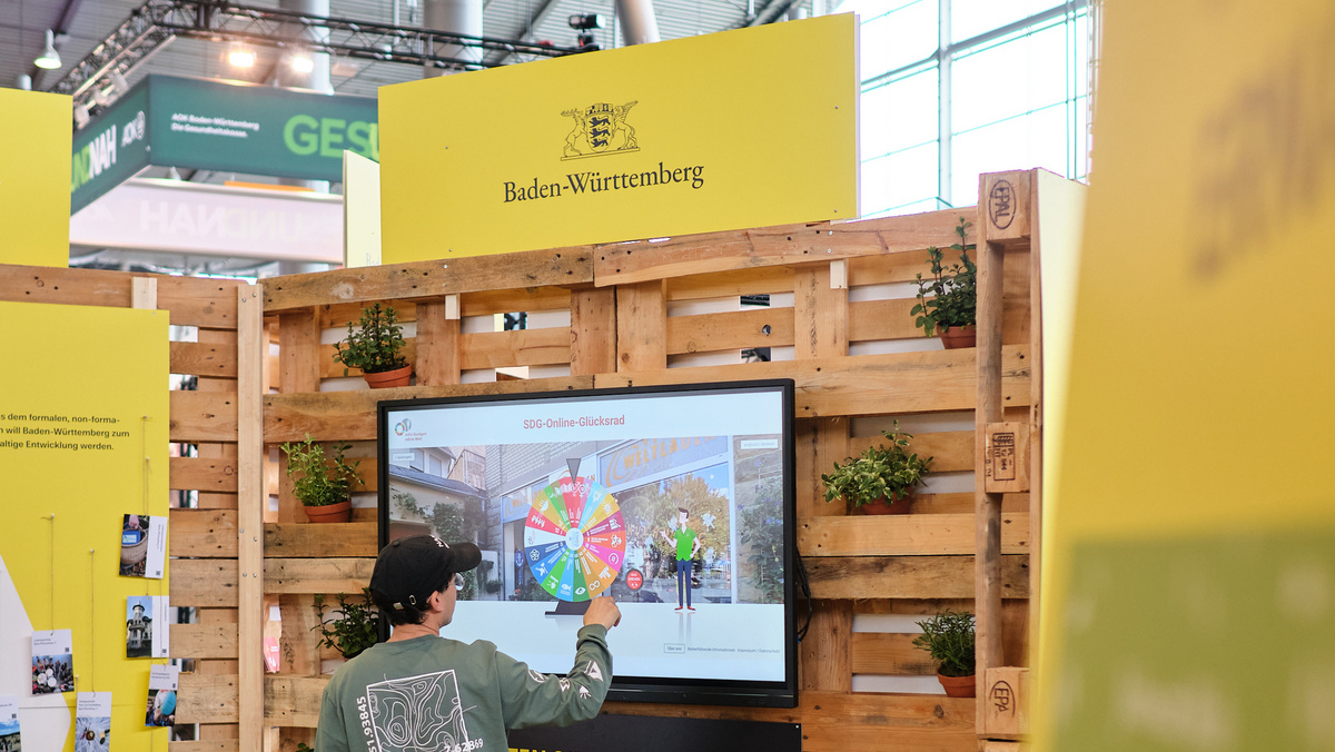 Ein Besucher dreht am digtalen SDG-Glückrad auf einem Touchscreen der KLIMA.LÄND.LOUNGE.