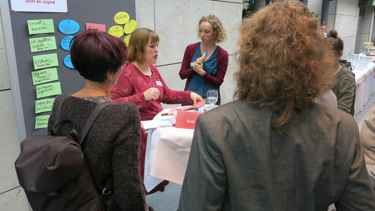 Fünf Frauen stehen bei einem Workshop diskutierend um einen Stehtisch herum. 