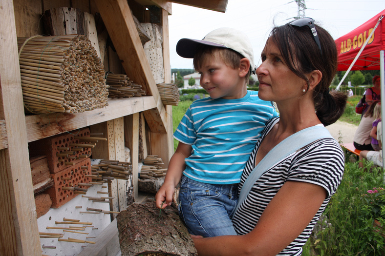 Frau mit Kind bestaunt Wildbienenkästen im Garten der Firma Albgold