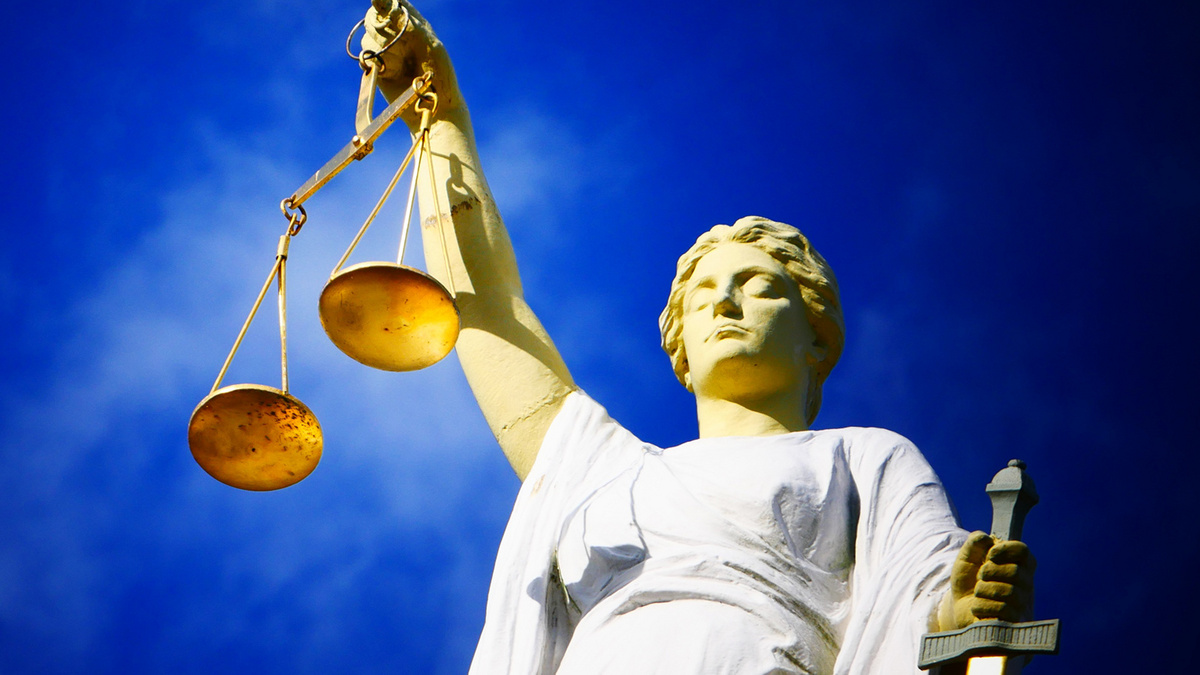 Justitia Vor einem tiefblauen Himmel hält eine Statue "Justita" mit dem rechten Arm eine Waagschale in die Höhe, in der linken Hand hält sie ein Schwert.