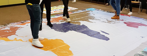 Sechs Schüler und eine Schülerin im Nachhaltigkeitsraum der Andreas-Schneider-Schule, auf dessen Boden eine Weltkarte liegt.
