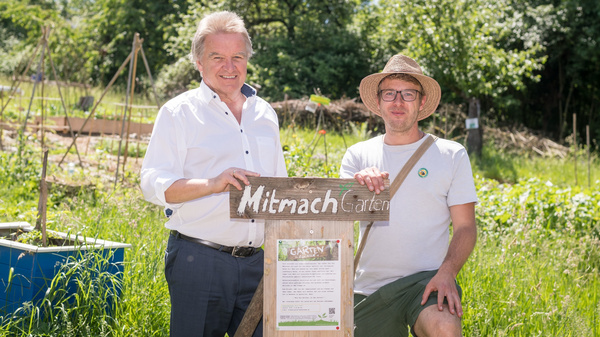 Minister Franz Untersteller posiert für ein Foto in einem Garten mit einem Mann, auf einem Schild steht "Mitmach Garten"