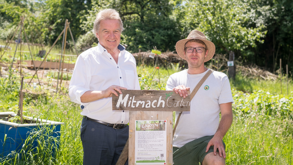 Minister Franz Untersteller posiert für ein Foto in einem Garten mit einem Mann, auf einem Schild steht "Mitmach Garten"