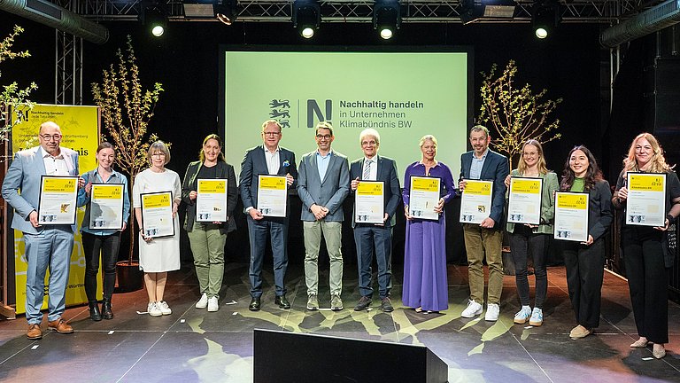 Die Vertreter und Vertreterinnen der neuen Klimabündnis BW Unternehmen stehen mit Staatssekretät Andre Baumann zu einem Gruppenbild zusammen mit ihren Urkunden in den Händen.