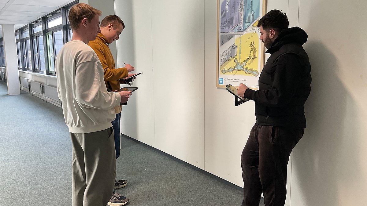 Drei Jugendliche stehen vor einem Plakat und schreiben etwas auf, sie nehmen an der Rallye teil.