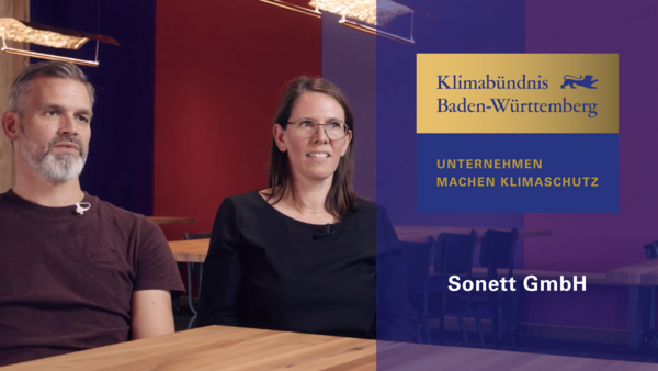 Rechts das Logo in gold und blau Klimabündnis Baden-Württemberg, Unternehmen machen Klimaschutz" und die Aufschrift Sonett GmbH. Links Oliver Groß und Rebecca Kramer, Geschäftsführer(in) des Unternehmens. 