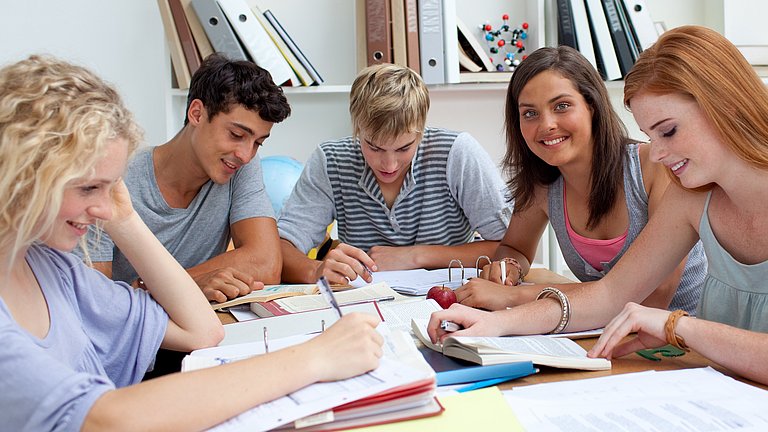 Fünf Jugendliche sitzen gemeinsam am Tisch, lesen oder arbeiten in Ordnern.