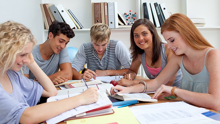 Fünf Jugendliche sitzen gemeinsam am Tisch, lesen oder arbeiten in Ordnern.
