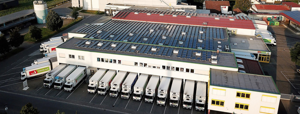 Eine Luftaufnahme des Firmengeländes der Früchte Jork GmbH. Auf den Dächern ist die Photovoltaik-Anlage erkennbar und im Hintergrund die Allgäuer Landschaft.