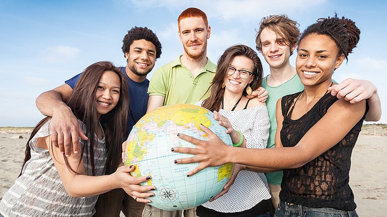 Junge Menschen unterschiedlicher Herkunft halten gemeinsam eine Weltkugel.