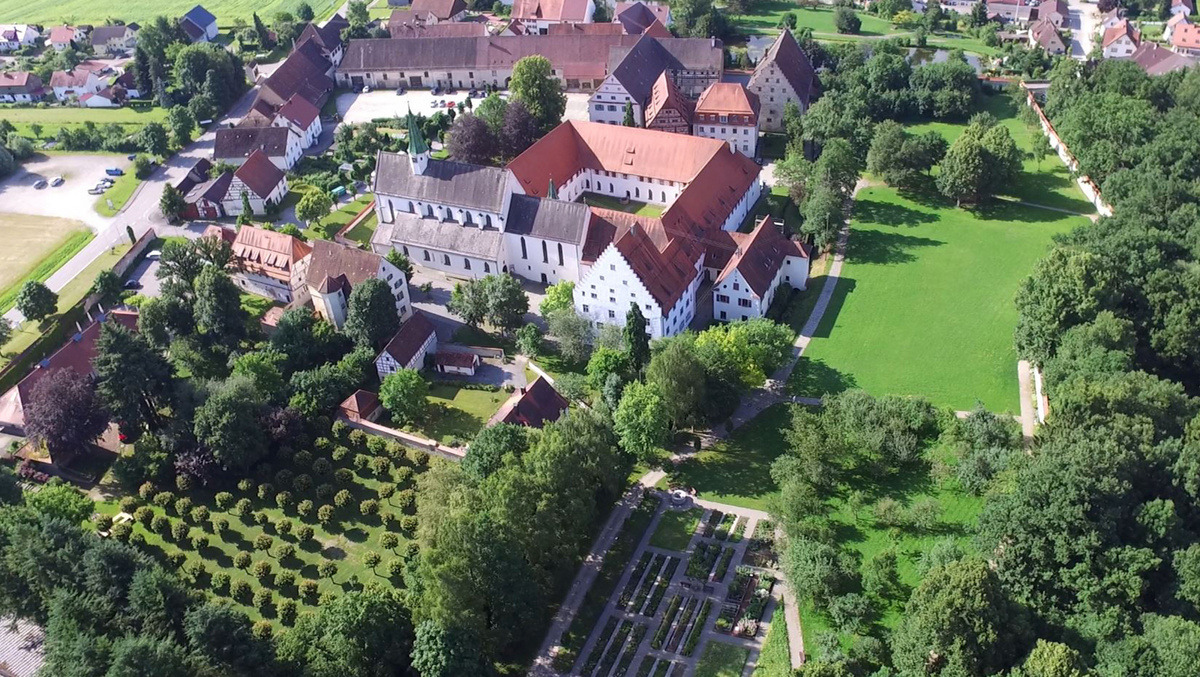 Luftaufnahme von der Klosteranlage Heiligkreuztal. Rechts im Bild sieht man ein großes grünes Spielfeld, links davon die Klostergebäude.