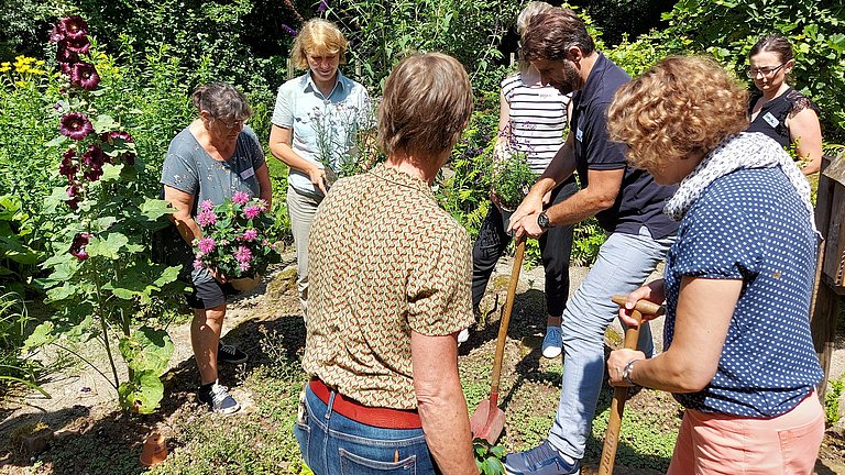 Mehrere Personen stehen in einen Garten zusammen und pflanzen Blumen.