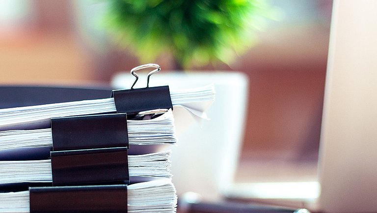 Ein Stapel zusammengefasster Dokumente liegen auf einem Arbeitstisch.