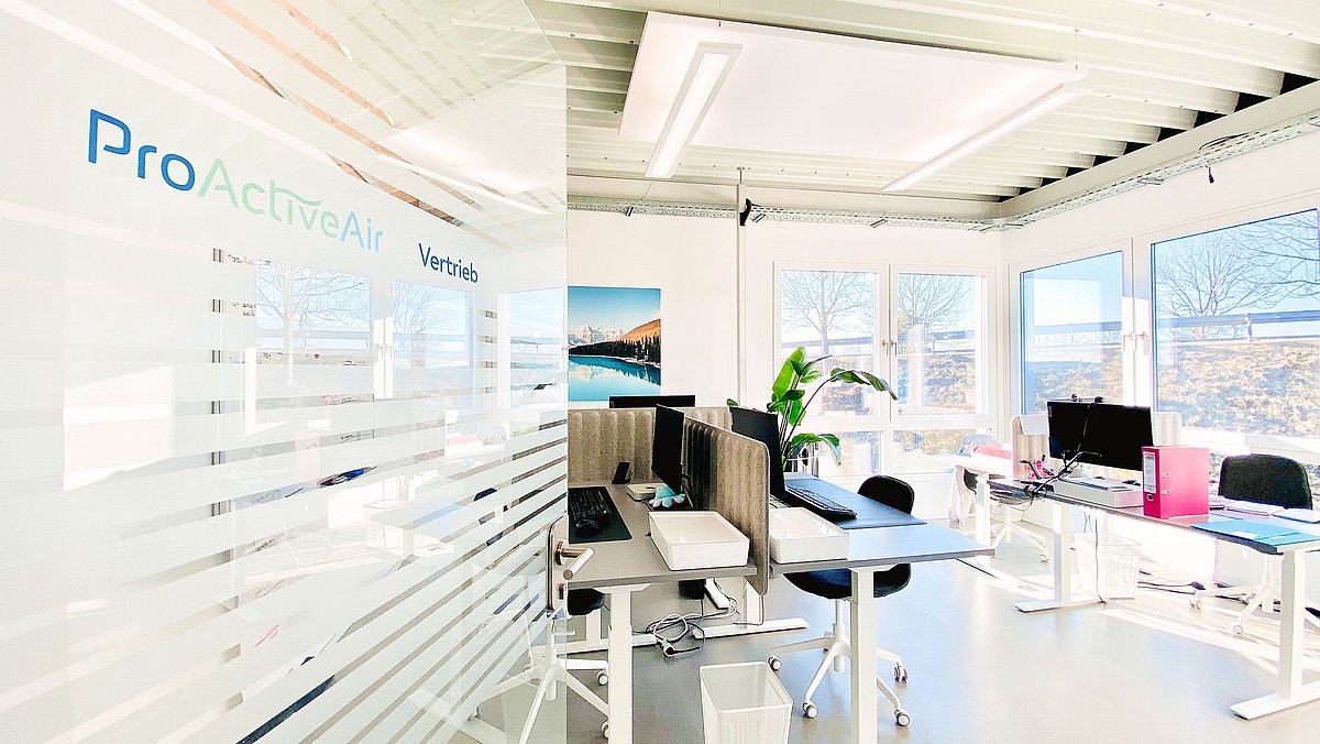 Ausschnitt eines Büros der ProActiveAir GmbH mit Schreibtischen, Stühlen und großen Fenstern.