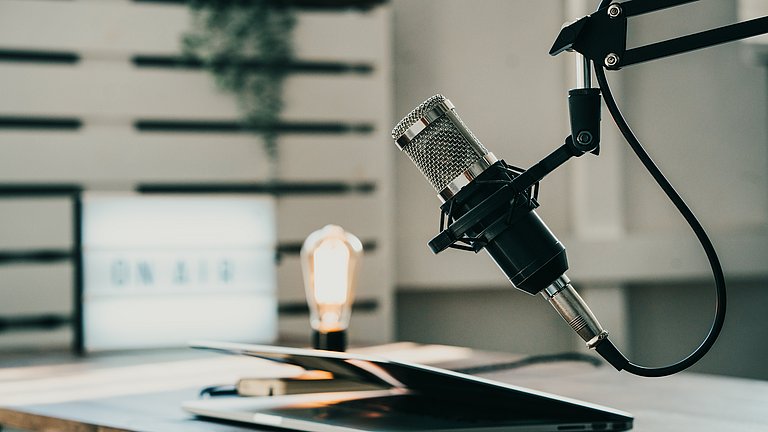 Ein Heimstudio für die Produktion von Podcasts mit Mikrophon und zugeklapptem Laptop.