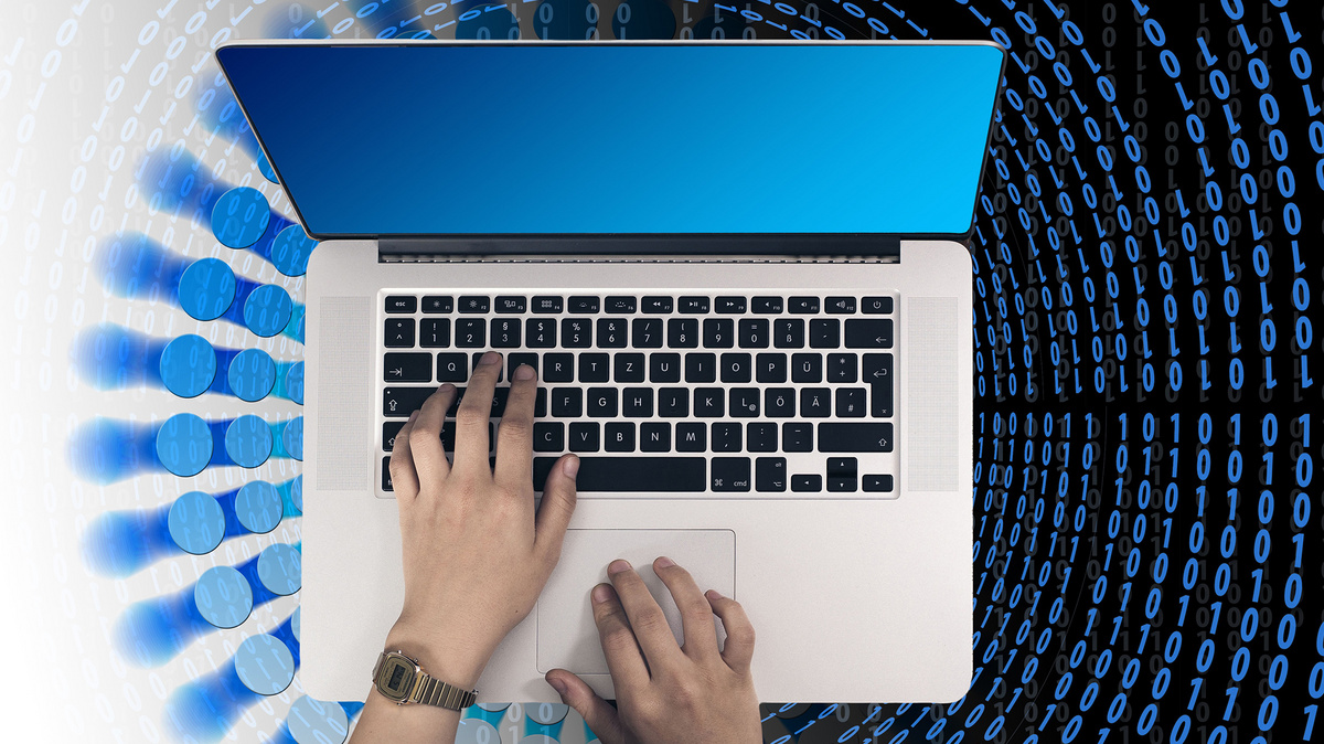 IT-Einsatz Zwei Hände bedienen einen aufgeklappten Laptop. Der Blick geht von oben auf den Laptop, der auf einem mit binären Zahlencode stilisiertem Untergund steht.