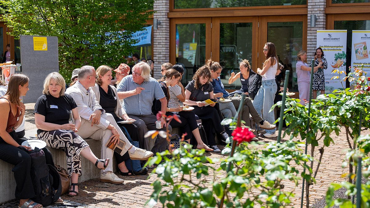 BNE-Festival Besucherinnen und Besucher unterhalten sich und lachen bei Sonnenschein im Innenhof.