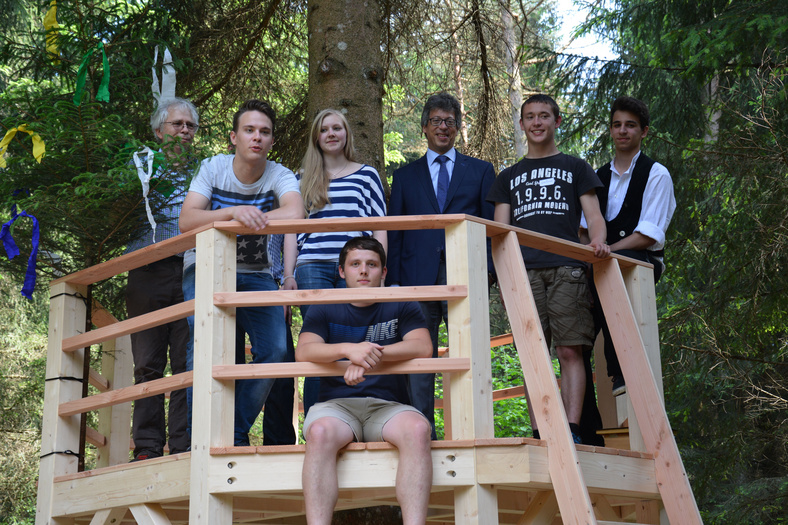 Gruppenfoto der Azubis des SchwörerHaus KG sitzen für das Foto in eigenerbautem Hochsitz im Azubiwald