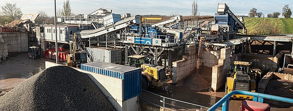 Eine blaugraue, stählerne Anlage, umgeben von Baustoffen, unter einem klaren, blauen Himmel.