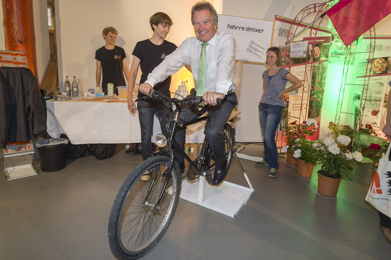 Franz Untersteller sitzt auf einem Fahrrad am Stand der Jugendinitiative 