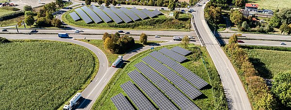 Luftaufnahme von Autobahnauf- und -ausfahrten mit Solarpanelen auf Grünflächen (sogenannte Innenohren). Umgeben von Straßen, Feldern und vereinzelten Gebäuden.