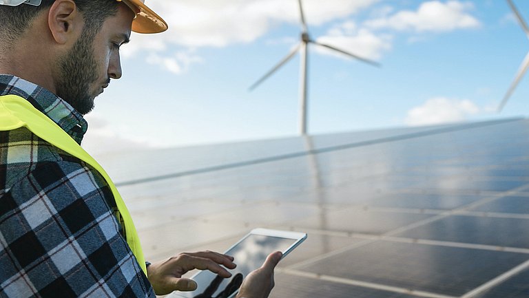 Ein Mann arbeitet mit einem digitalen Tablet im Umfeld einer Photovoltaikanlage.