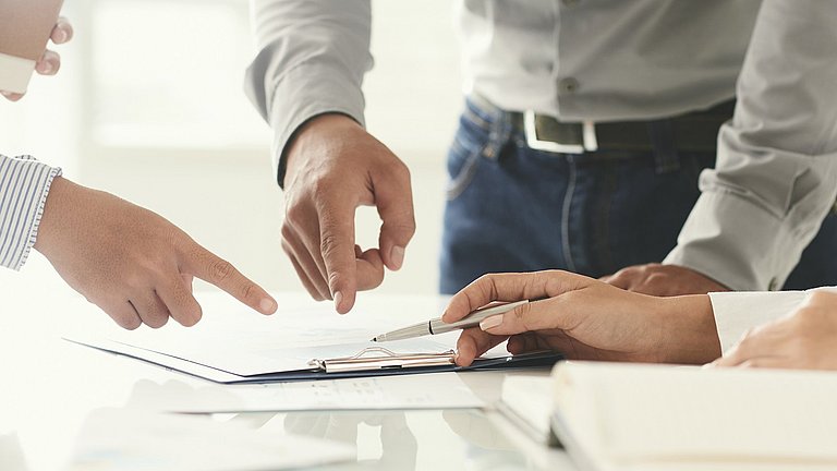 Mehrere Hände zeigen auf Dokumente auf einem Tisch.