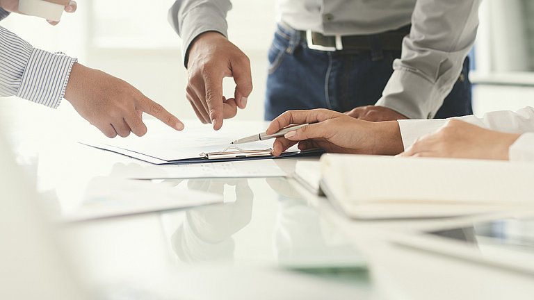 Mehrere Hände zeigen auf Dokumente auf einem Tisch.