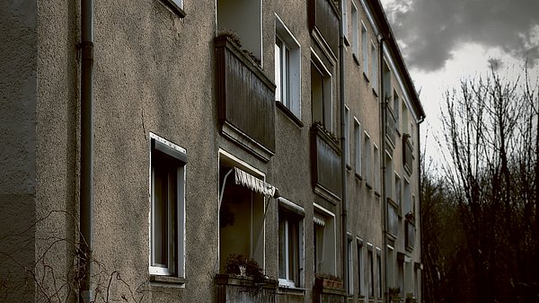 Dargestellt ist eine graue und ungepflegte Fassade eines Mietshauses.