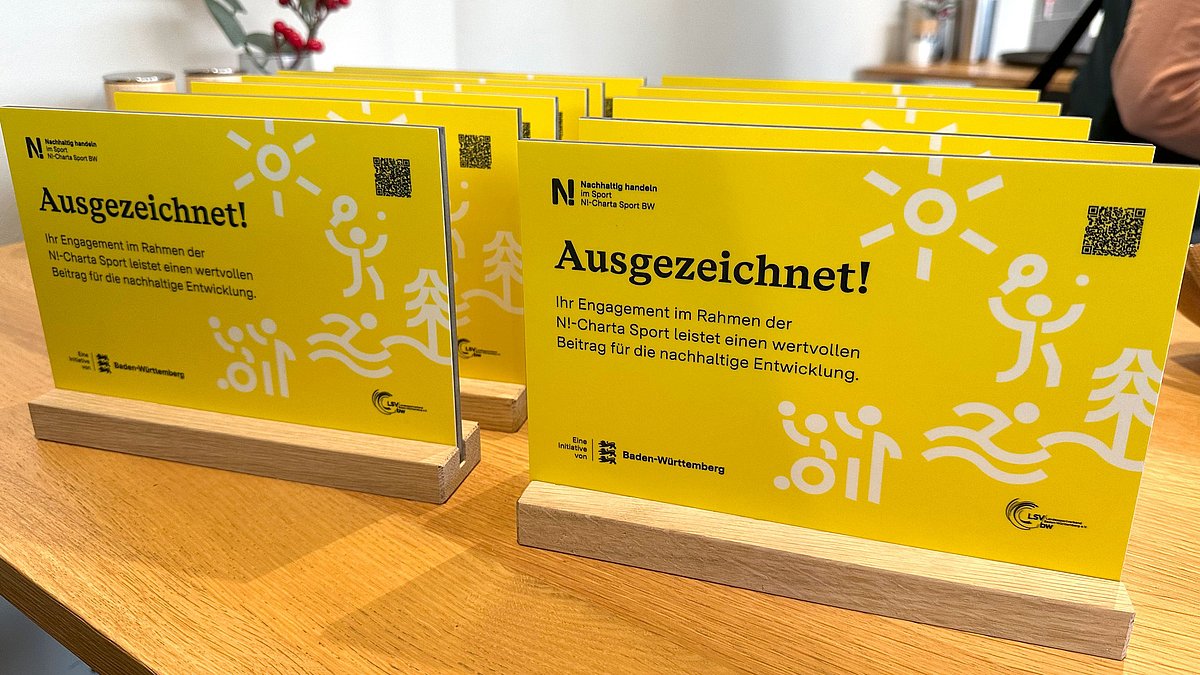 Plaketten für die Ehrung des Engagements der N!-Charta Sport mit der Aufschrift „Ausgezeichnet" im gelben Landes-CD von Baden-Württemberg