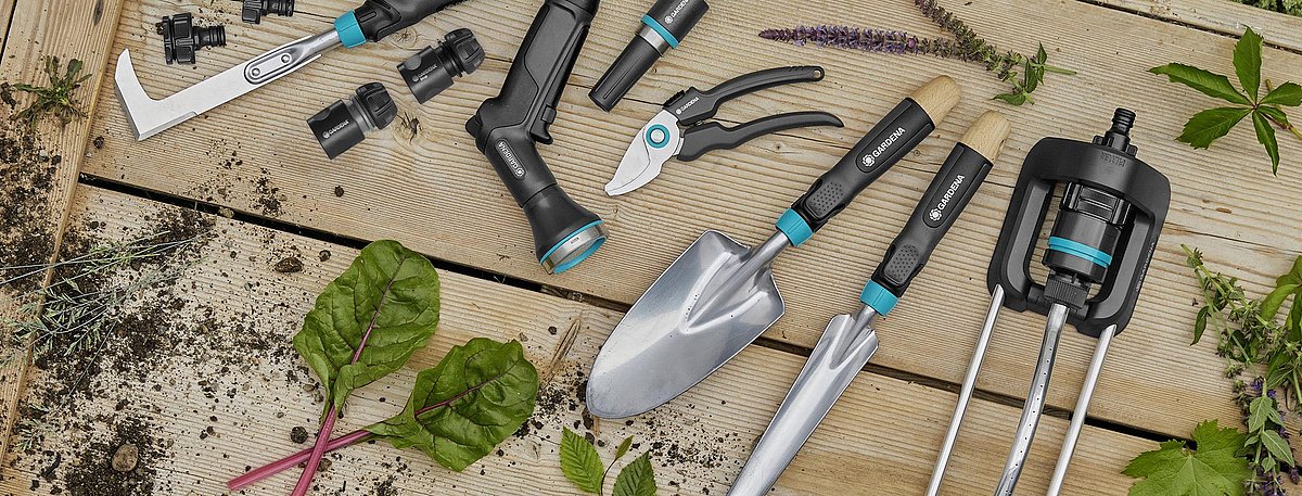 Eine Auswahl verschiedener Gartenhandgeräte liegen aufgereit auf einem Brett.