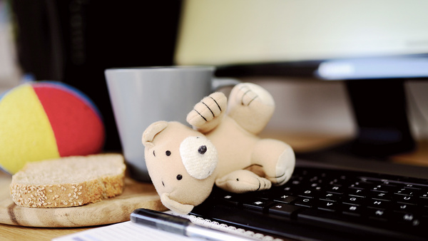 Auf einer Computertastatur liegt ein Stofftier, daneben ein Vesperbrett mit einer Scheibe Brot, ein Stoffball und ein Kaffebecher.