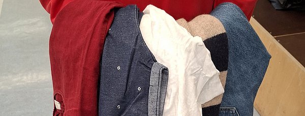 Mehrere Kleidungsstücke in der Hand einer Frau.