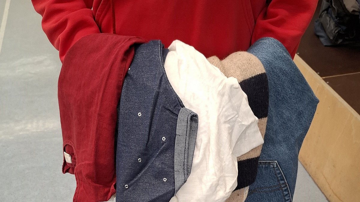 Mehrere Kleidungsstücke in der Hand einer Frau.