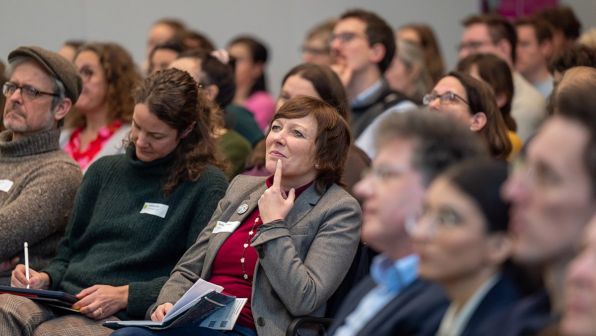 Menschen aus dem Publikum schreiben sich Notizen und hören konzentriert zu.