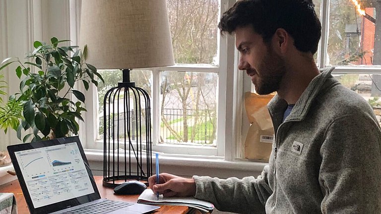 Erwachsener Mann, der an einem Laptop sitzt und sich notizen macht.