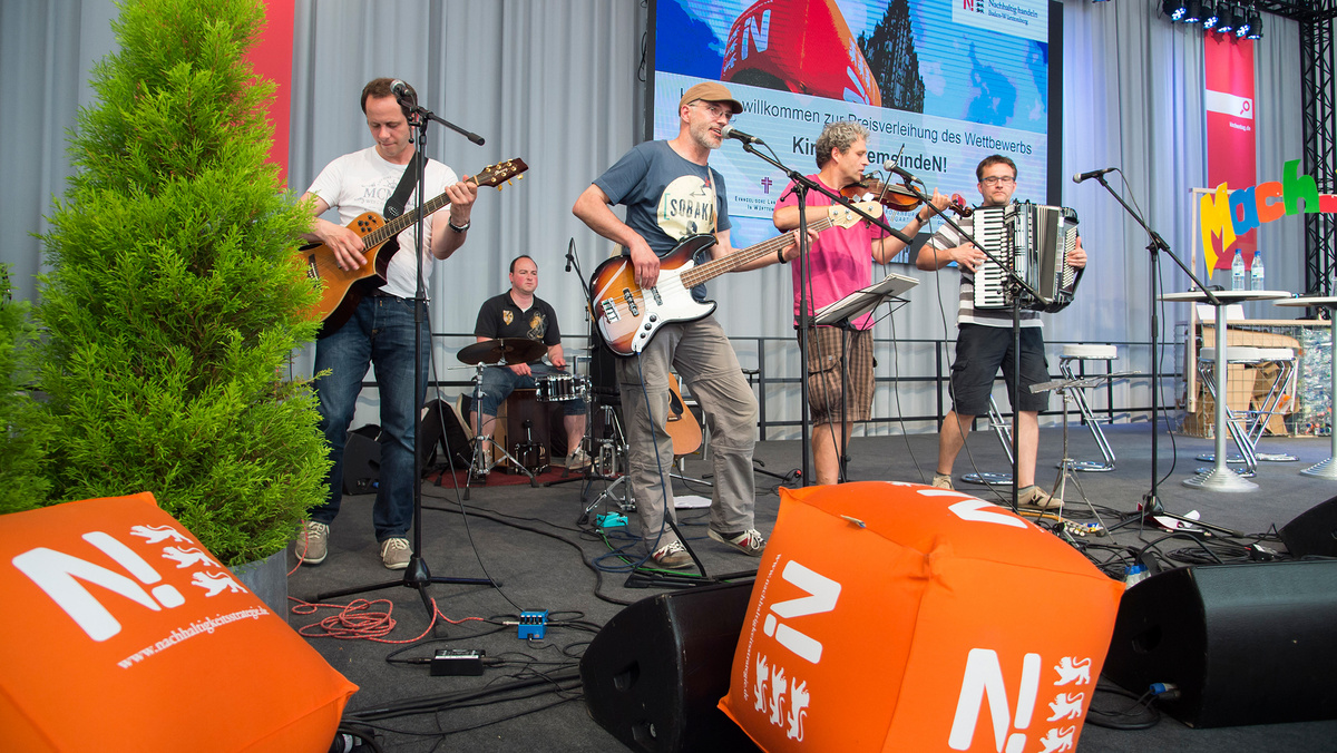 Fünf Musiker mit Gitarren, Geige, Akkordeon und Schlagzeug sorgen beim Deutschen Ev. Kirchentag in Stuttgart auf der Bühne der Nachhaltigkeitsstrategie  für Unterhaltung.