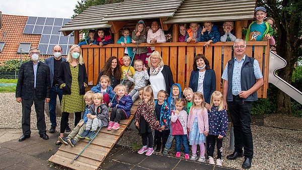 Eine Gruppe von Erwachsenen und Kindern im Kindergartenalter, die auf vor und auf einer Hütte stehen und in die Kamera blicken.