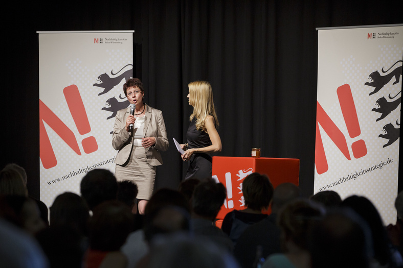 Nachhaltigkeitstage 2014 Eine Frau auf der Bühne spricht ins Mikrofon. Die Moderatorin neben ihr sieht sie währenddessen an.
