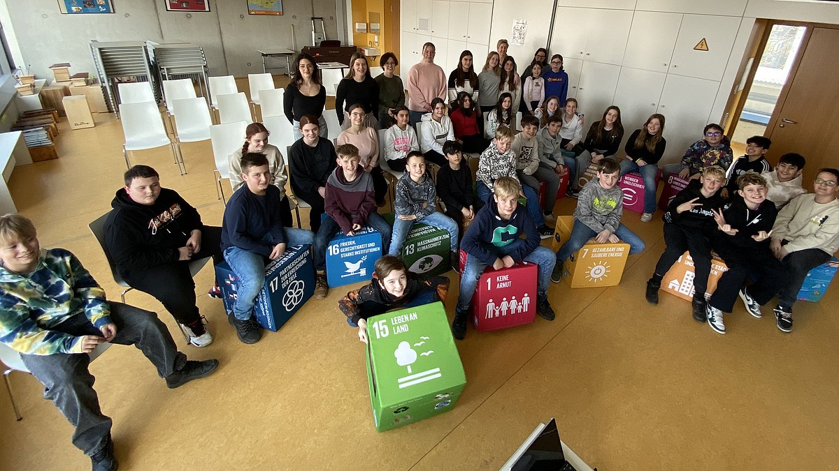 Schulklasse sitzt auf den SDG-Sitzwürfeln.