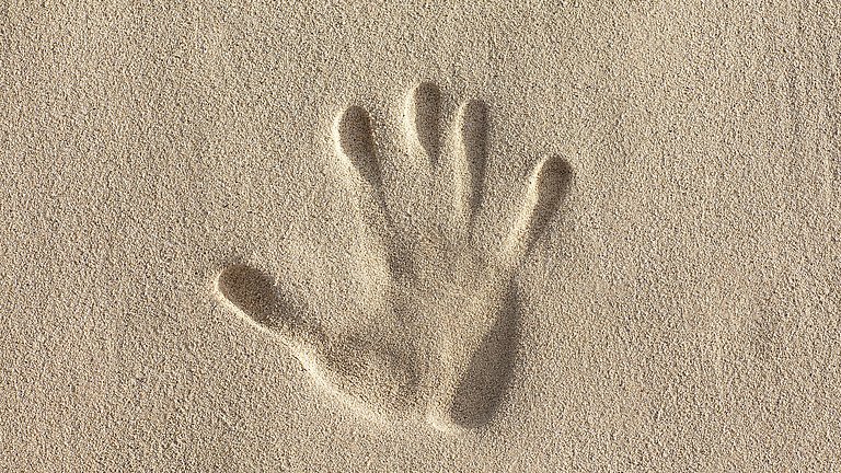 Ein Abdruck einer rechten Hand im Sand.