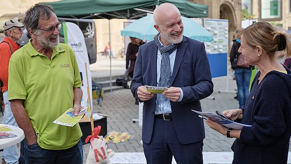 Zwei Männer und eine Frau stehen in einer Reihe und lächeln sich an.