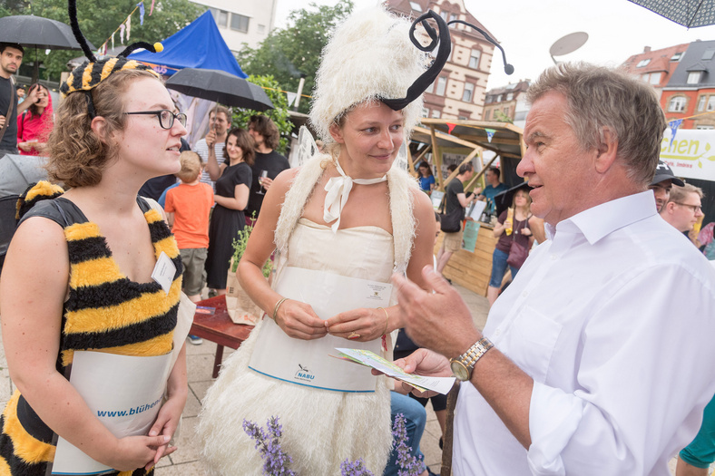 Herr Minister Franz Untersteller unterhält sich mit zwei Frauen, die sich als zwei Insekten verkleidet haben, auf dem Übermorgen Markt