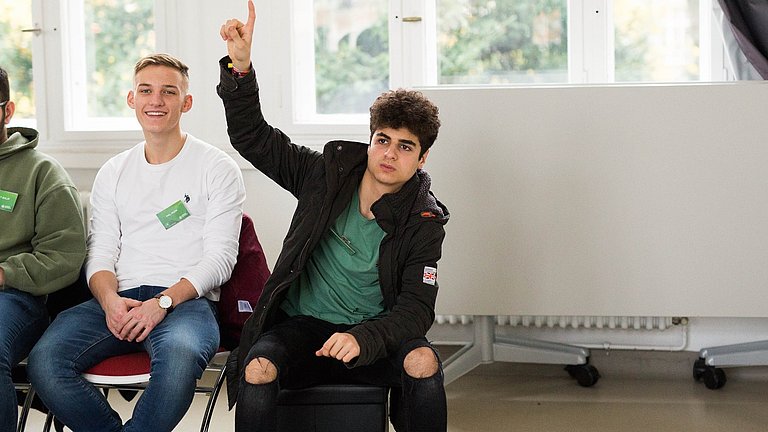 Nahaufnahme von zwei Schülern von denen einer die Hand hebt.