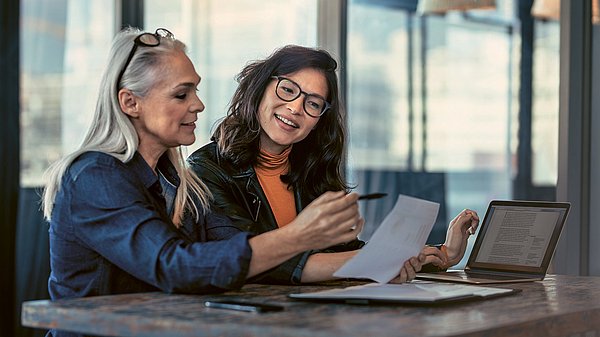 Dargestellt ist eine ältere Frau, die mit einer Mitarbeiterin etwas analysiert.