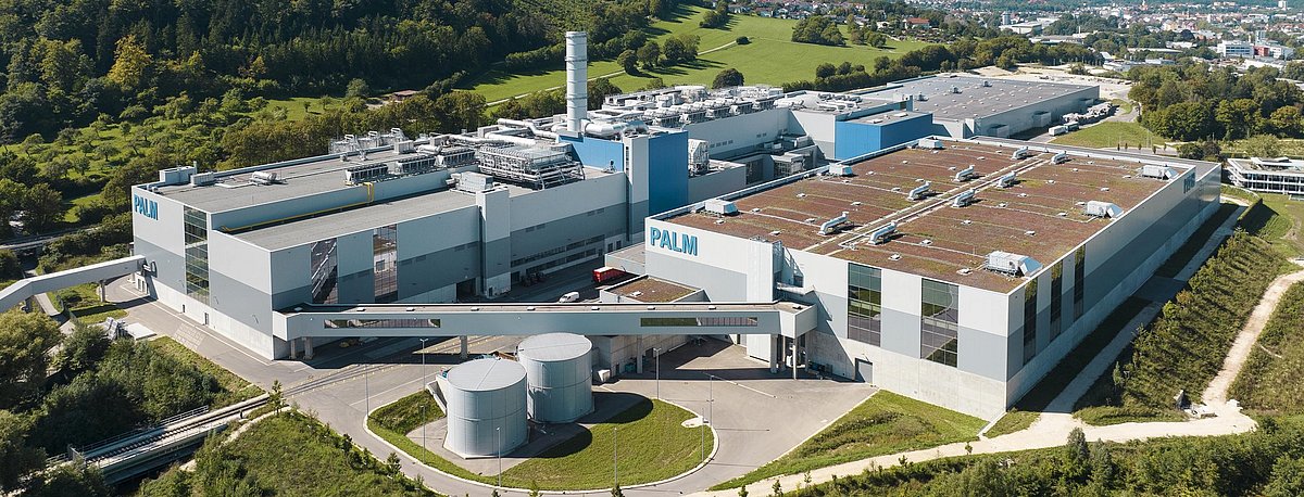 Luftbild der neuen Papierfabrik am Stammsitz der Papierfabrik Palm in Aalen. Man erkennt die Halle mit der Papiermaschine PM 5, den Steg zum Rollenlager sowie das Rollenlager selbst. Im Hintergrund und im Vorfeld der Papiermaschinenhalle sind das Rohstofflager für Altpapier und die Stoffaubereitung zu sehen. Am rechten Bildrand erkennt man zudem die zentrale Verwaltung von PALM.