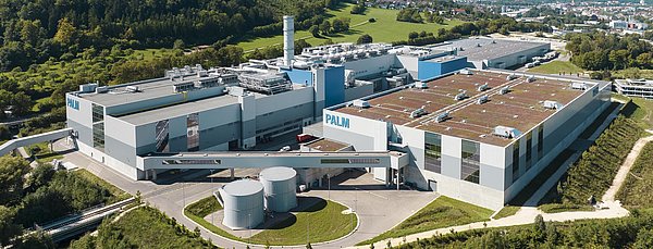 Luftbild der neuen Papierfabrik am Stammsitz der Papierfabrik Palm in Aalen. Man erkennt die Halle mit der Papiermaschine PM 5, den Steg zum Rollenlager sowie das Rollenlager selbst. Im Hintergrund und im Vorfeld der Papiermaschinenhalle sind das Rohstofflager für Altpapier und die Stoffaubereitung zu sehen. Am rechten Bildrand erkennt man zudem die zentrale Verwaltung von PALM.
