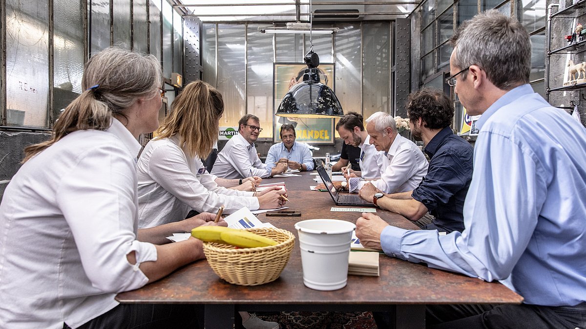 Verschiedene Leute sitzen zusammen bei einer Besprechung an einem Tisch.