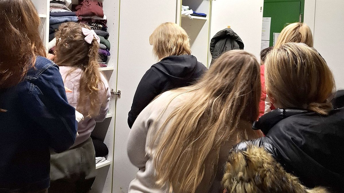 Menschen stehen vor den Kleiderschränken und suchen nach passenden Kleidern.