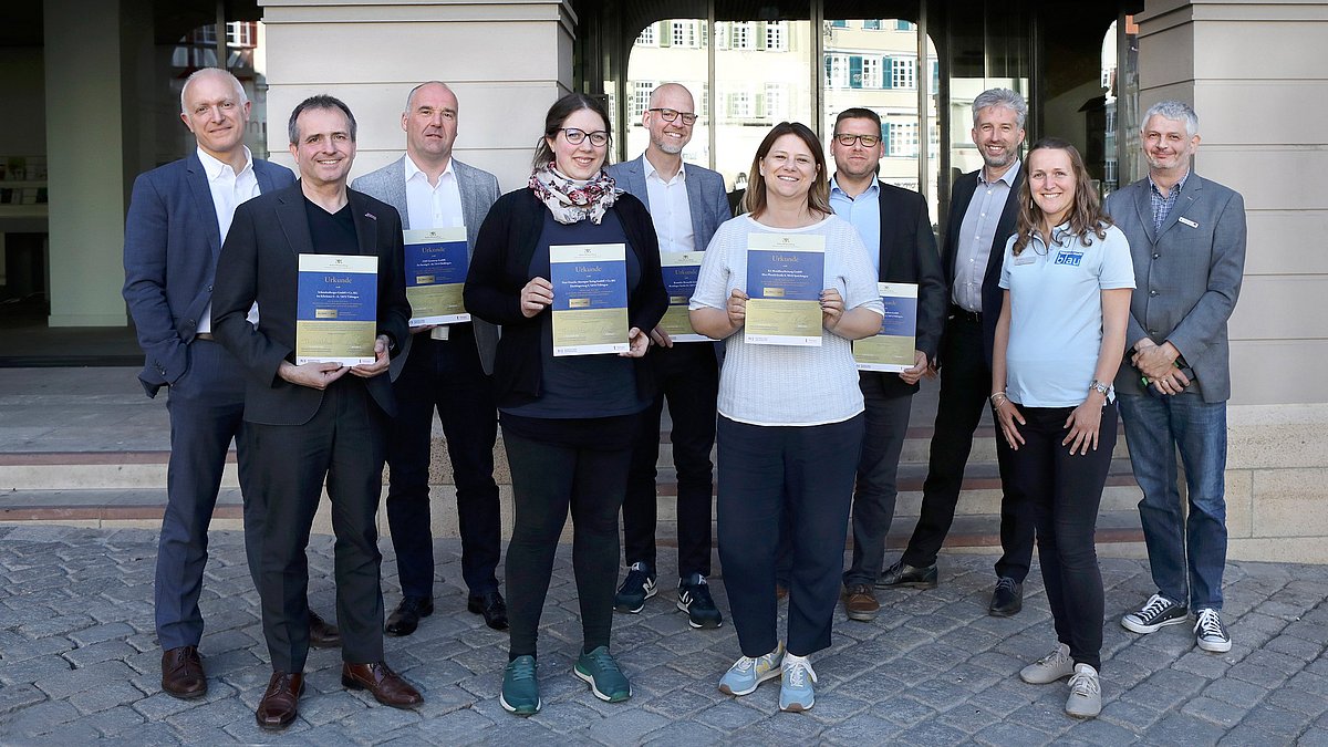 Teilnehmende aus dem Pilotptojekt Klimafit stehen als Gruppe zusammen und zeigen ihre Urkunde, mit der sie zu einem Klimafit-Betrieb ausgezeichnet wurden.